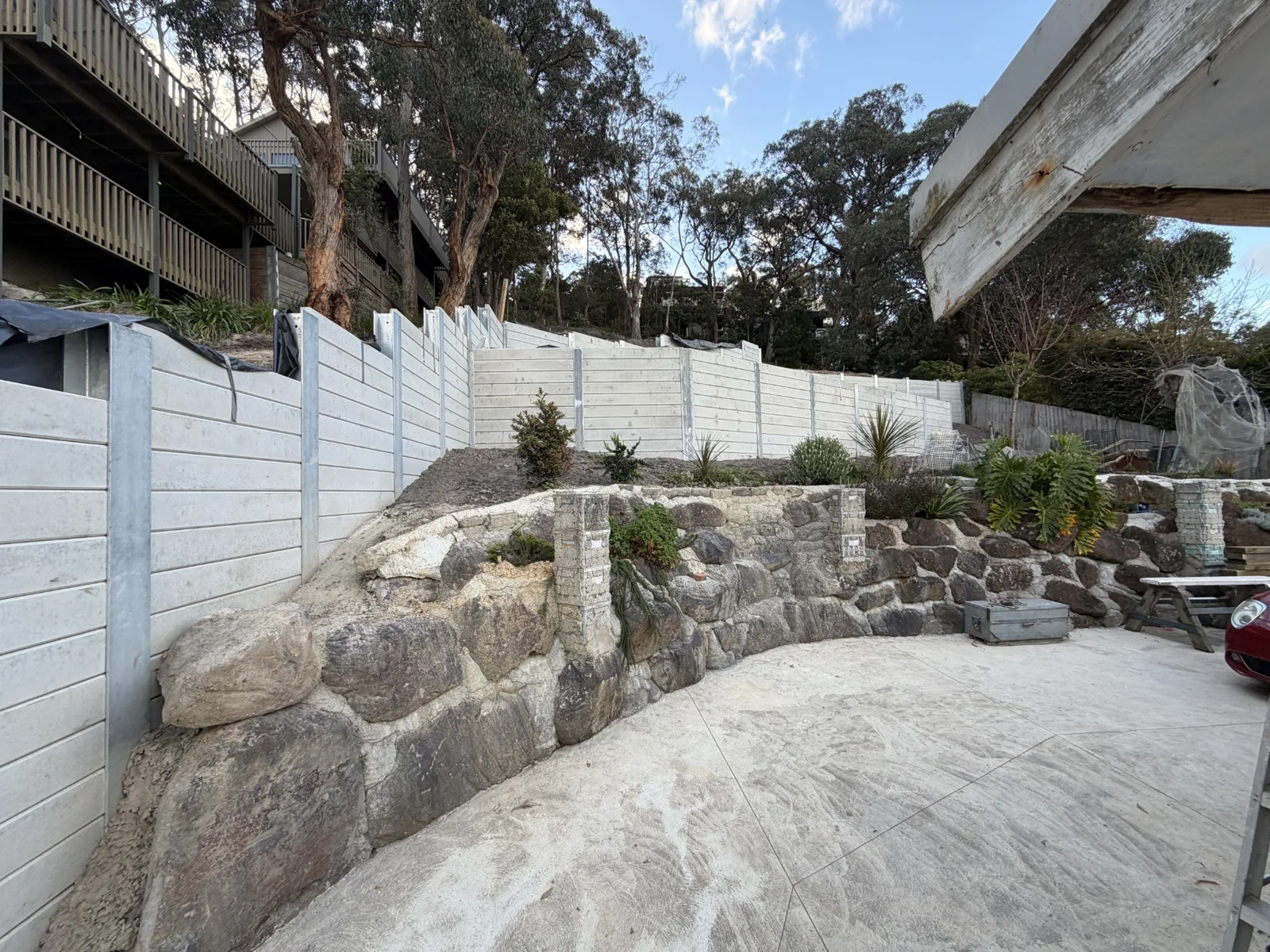 Concrete sleeper retaining wall runs stepping across a steep Lorne property above an existing stone wall