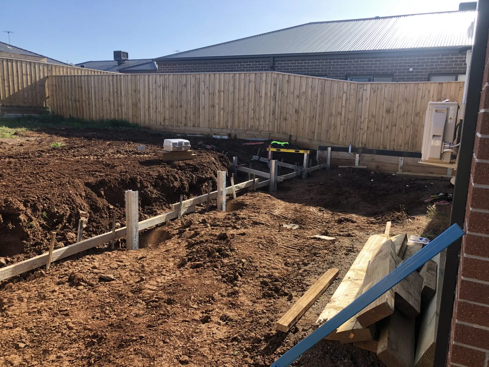 Residential excavation with retaining wall posts and timber formwork beside a house